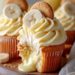Close-up of banana pudding cupcakes topped with banana buttercream, mini vanilla wafers, and banana slices, displayed on a rustic wooden board.