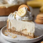 Unbaked creamy banana pudding cheesecake in a foil-wrapped springform pan, placed inside a roasting pan for a water bath on a rustic kitchen surface.