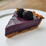 Slice of blackberry and lavender tart recipe on white plate with creamy purple filling and nut crust