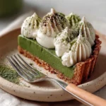 Green matcha white chocolate tart topped with whipped cream on a rustic plate