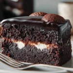 A slice of bumpy cake with rich chocolate base, glossy fudge topping, and visible vanilla buttercream bumps, served on a white plate.