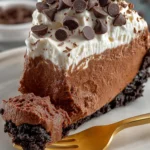 Slice of chocolate Jello pudding pie with Oreo crust and Cool Whip topping, topped with chocolate chips and served on a white plate