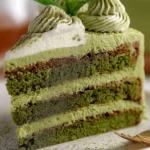 Triple-layer matcha cake slice with creamy whipped frosting and piped matcha topping on a white plate, rich and fluffy.