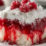 Moist Raspberry Zinger Poke Cake slice topped with Cool Whip and shredded coconut on a white plate