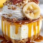 Close-up of banana cream pie slice with caramel drizzle, whipped cream, fresh banana slices, and pecans on graham cracker crust