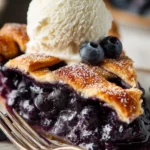 Slice of blueberry pie recipe with golden flaky crust and vanilla ice cream on top