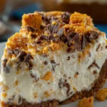 A thick slice of no-bake Butterfinger pie with crushed candy topping and creamy peanut butter filling in an Oreo crust
