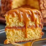 Close-up of a moist Southern caramel cake slice with thick golden caramel icing and soft yellow layers, served on a dark plate with a golden fork