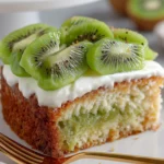 Moist kiwi cake slice topped with Greek yogurt frosting and fresh kiwi fruit on a white plate