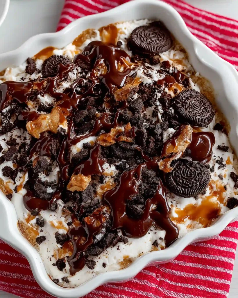 Crushed Oreos, chocolate cake mix, and caramel sauce drizzled in a white baking dish as the final layer of Oreo Dump Cake