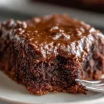 Moist slice of chocolate Texas sheet cake recipe with glossy warm frosting on a white plate